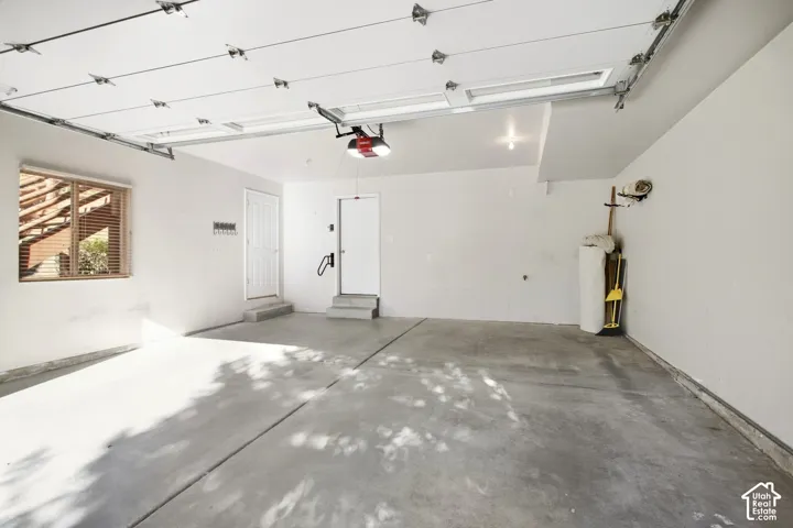 Attached garage with a concrete floor, window with blinds, and two entry doors