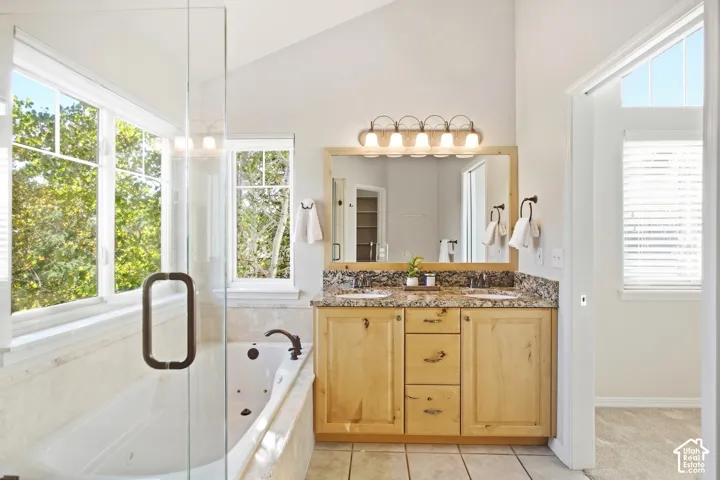 Vaulted ceiling bathroom featuring a jetted tub, glass-enclosed shower, dual vanity with granite countertop, and wood-finish cabinetry