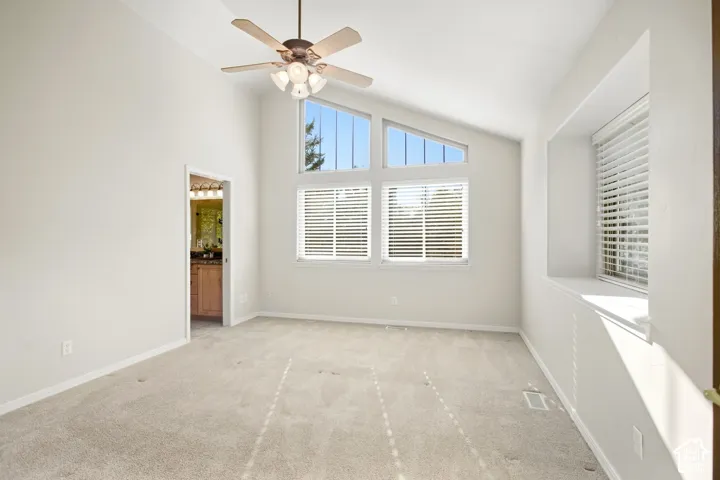 Vaulted ceiling with ceiling fan, multiple windows, window seat, and neutral carpeting
