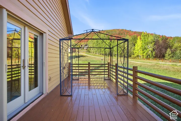 Wood-finish deck with a metal gazebo and wood railing, complemented by horizontal siding and glass-paneled double doors