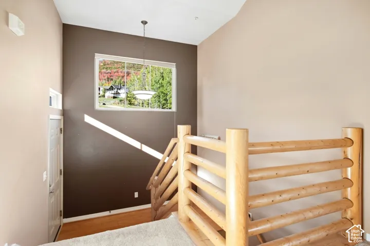 Vaulted ceilings, large picture window, wood-finish flooring, natural wood railing, and a pendant light fixture