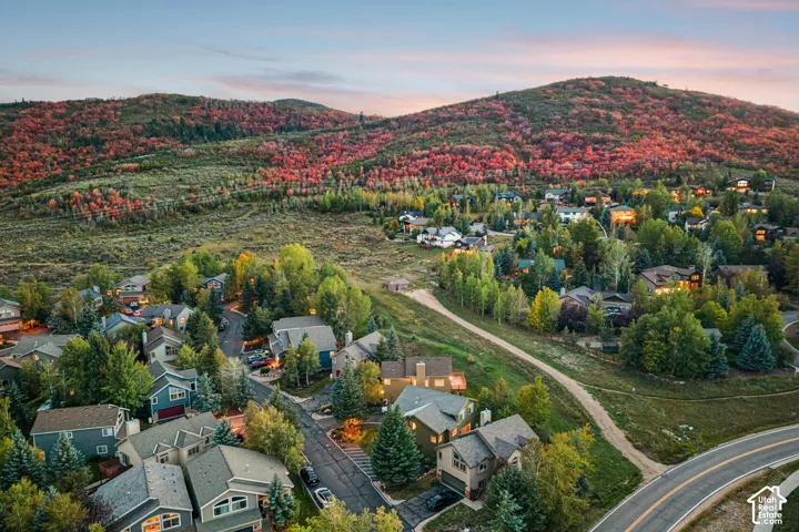Lush mountainous terrain with autumnal foliage surrounding a residential area, featuring an asphalt road and established trees