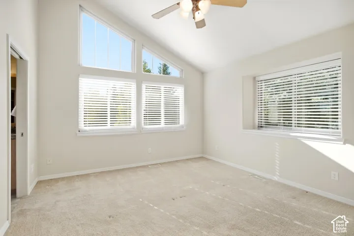 Vaulted ceiling featuring a ceiling fan with light fixture, neutral carpet flooring, and multiple windows with blinds
