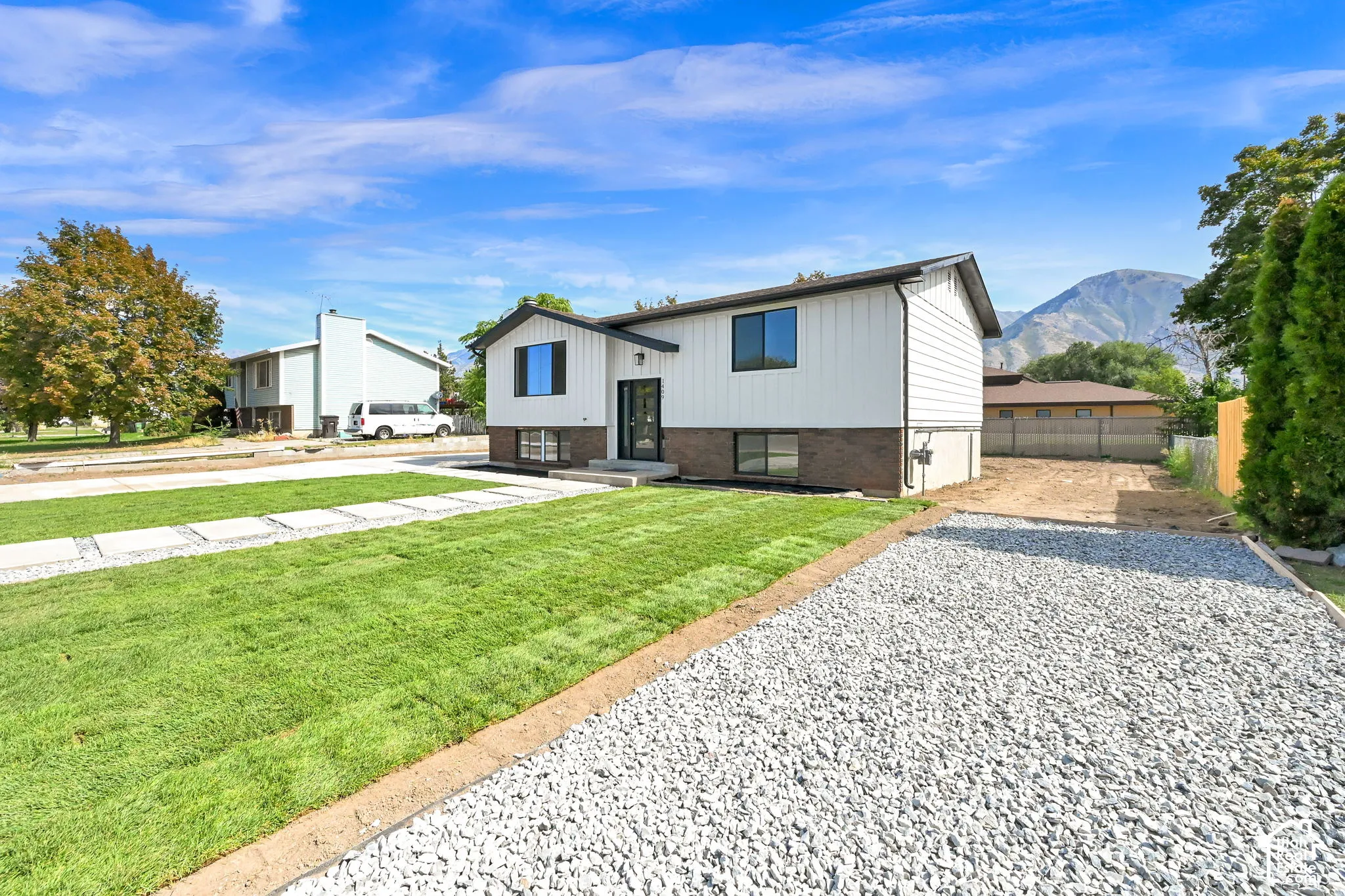 Exterior with white siding and dark trim, featuring a gravel driveway and a green lawn