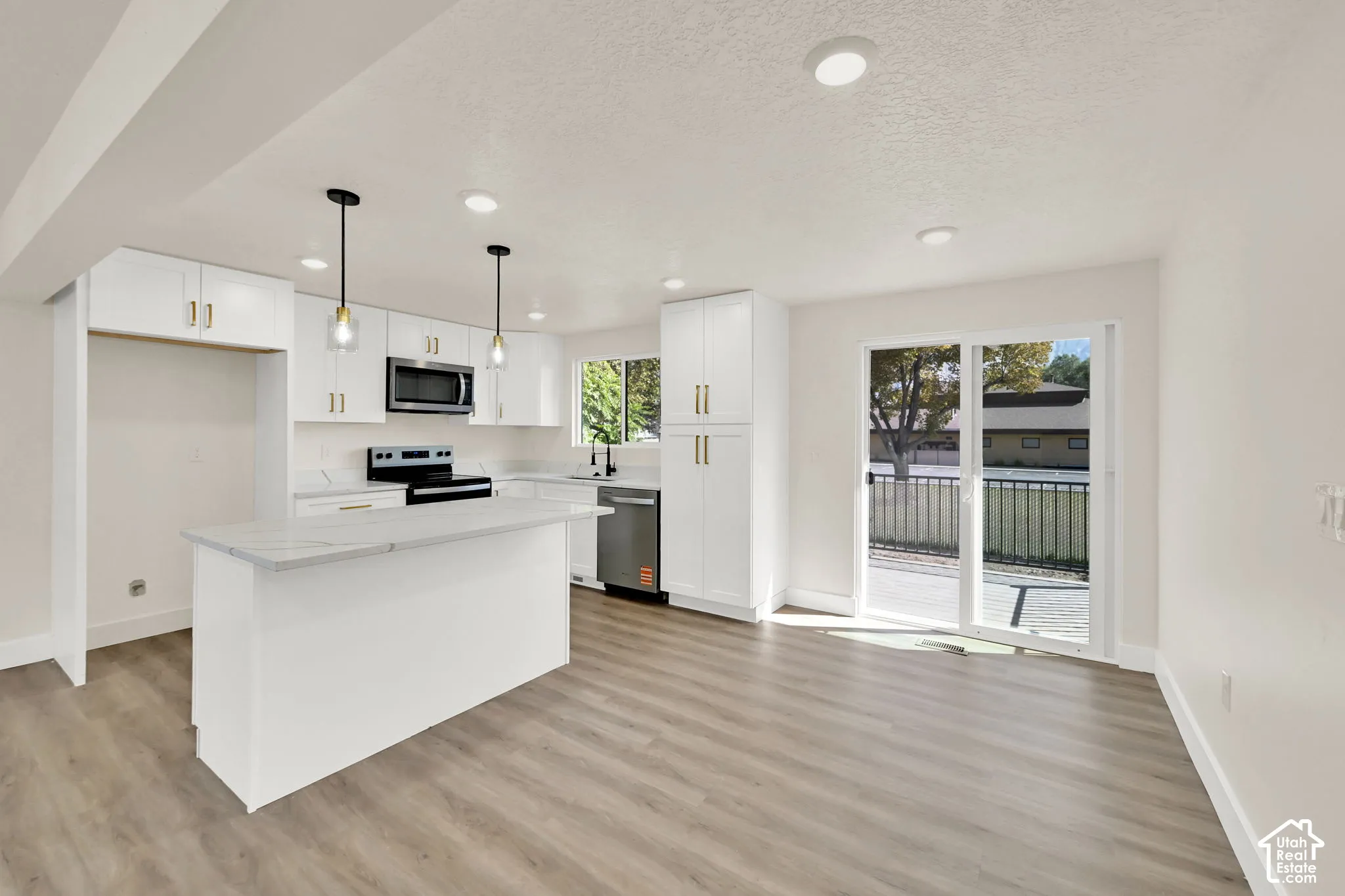 Modern kitchen featuring white cabinetry, a central island with a light-toned countertop, stainless steel appliances, and wood-finish flooring