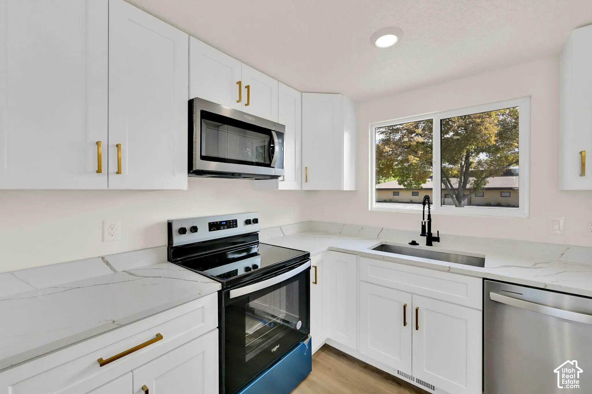 White shaker cabinetry with gold-finish hardware, stainless steel appliances, white countertops, and a stainless steel sink with a black-finish faucet