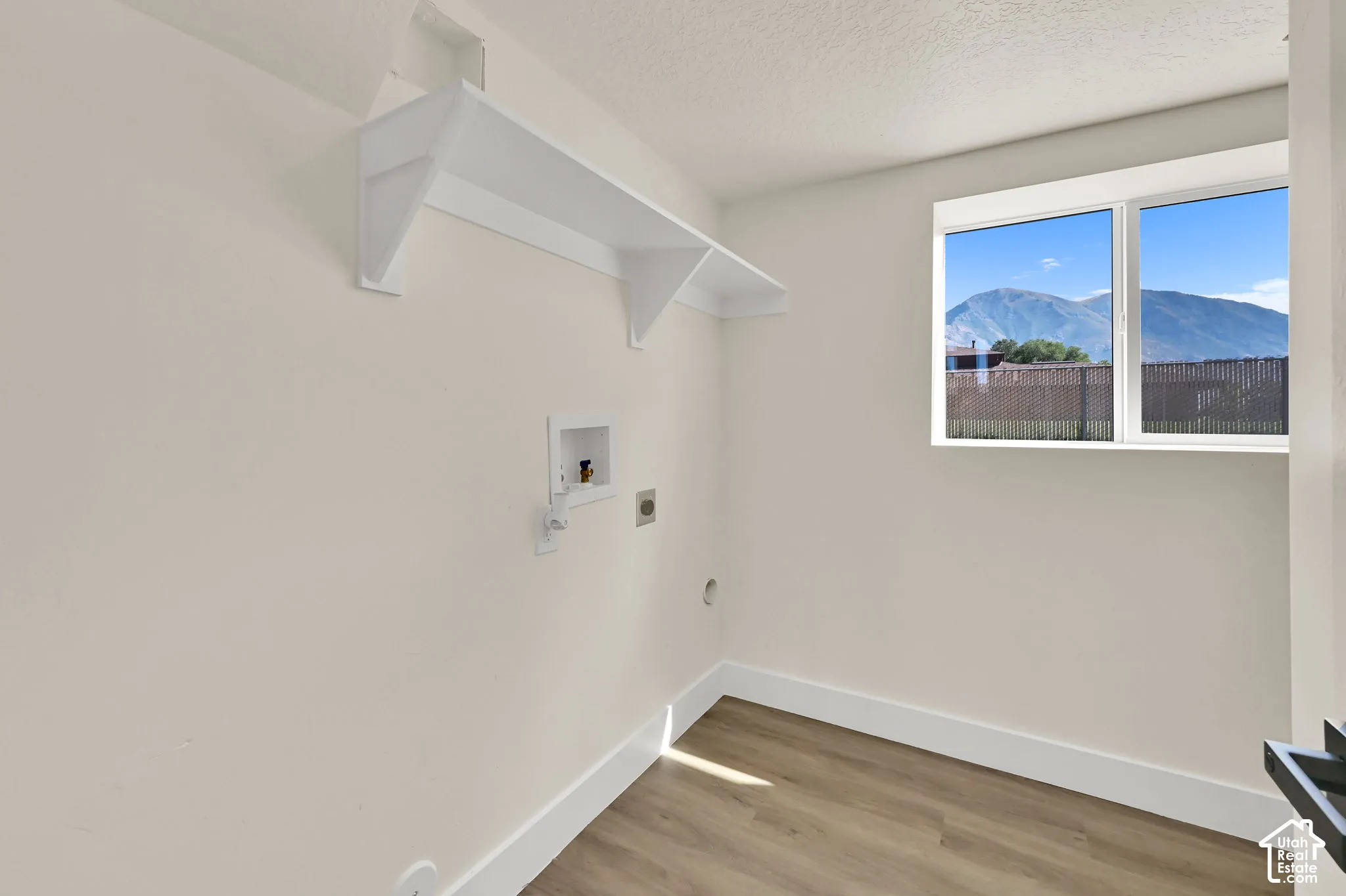 Laundry area featuring wood-finish flooring, a double-paned window, and a built-in wall shelf