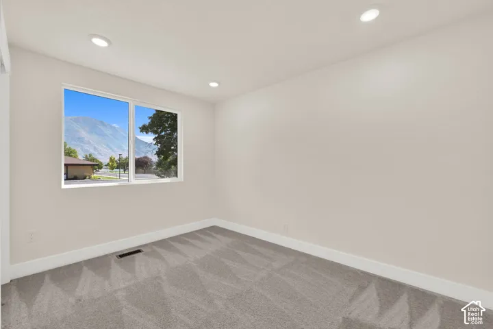 Recessed ceiling lighting, a large window, neutral wall tones, gray patterned carpeting, and white trim