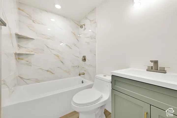 Bathtub with a tiled surround featuring built-in niches, a vanity with a light green finish, and a white countertop with an integrated sink