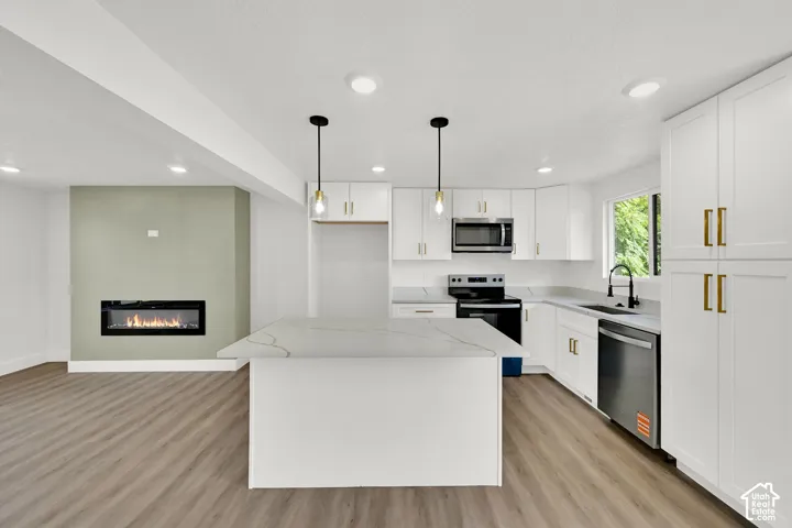 Open-concept kitchen and living area featuring white shaker cabinetry, an island with a light-toned countertop, and stainless steel appliances