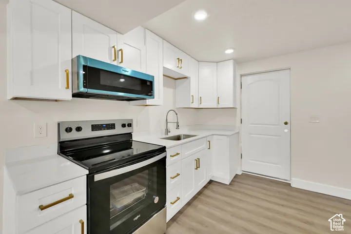 Full kitchen featuring white cabinetry, gold-finish hardware, stainless steel range with overhead microwave, and light-tone countertops