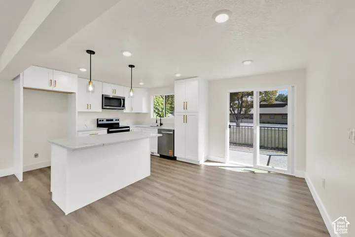 Modern kitchen featuring white cabinetry, a central island with a light-toned countertop, stainless steel appliances, and wood-finish flooring