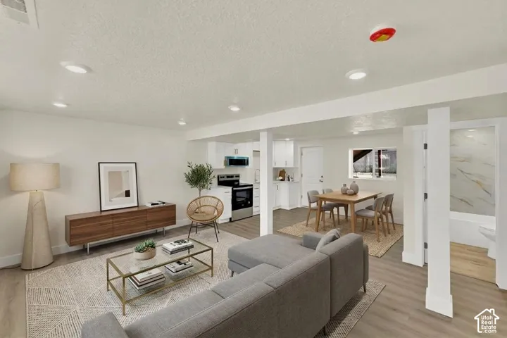 Open-concept living area featuring wood-finish flooring, recessed lighting, and a kitchen with white cabinetry and stainless steel appliances