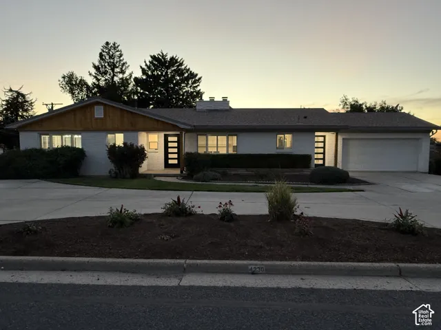 White brick exterior with wood-paneled gables, an attached garage, a paved driveway, and mature landscaping