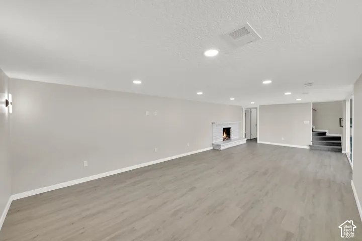 Expansive room featuring wood-finish flooring, a white brick fireplace, recessed lighting, and wall sconces