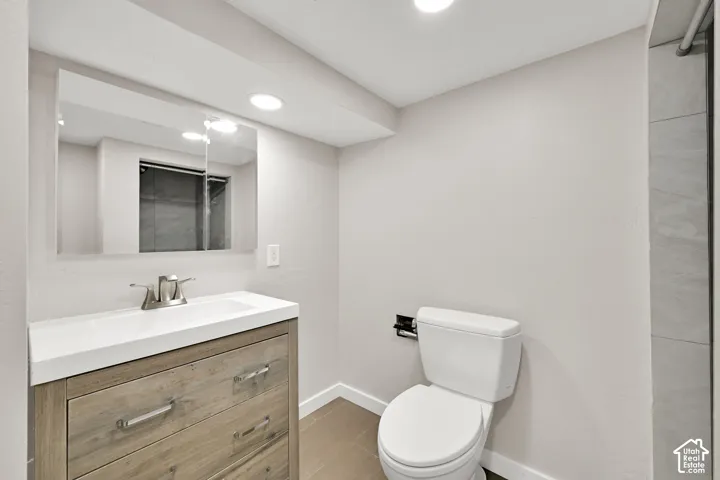 Recessed lighting illuminates a vanity with wood-finish cabinetry, a white countertop with an integrated sink, and a framed mirror