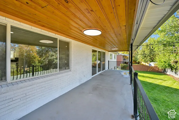 Covered outdoor patio with a wood-plank ceiling, recessed lighting, and a painted brick exterior
