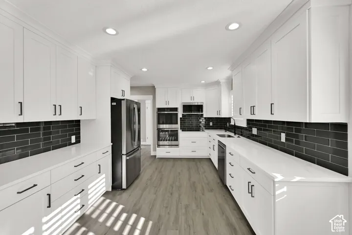 White shaker-style cabinetry with black hardware, complementing black subway tile backsplash, white countertops, and wood-finish flooring