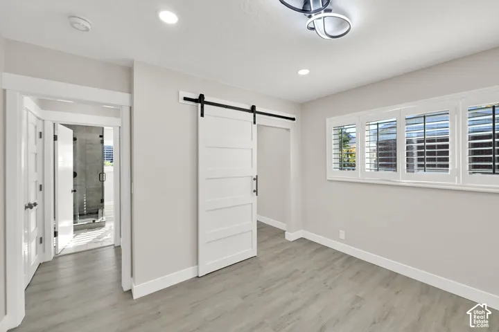 Light gray walls with white trim, wood-finish flooring, white plantation shutters, white barn door, and recessed lighting