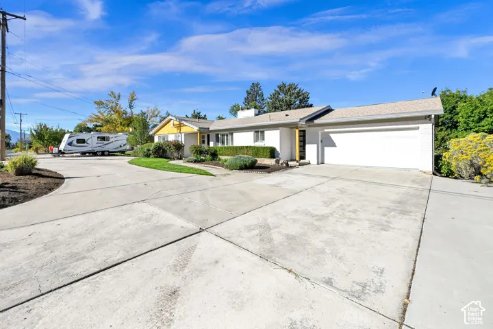 Expansive concrete driveway, attached two-car garage, manicured shrubs, and mature landscaping