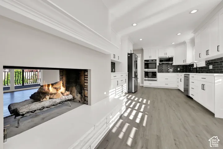 White cabinetry, recessed lighting, black subway tile backsplash, stainless steel appliances, and wood-finish flooring