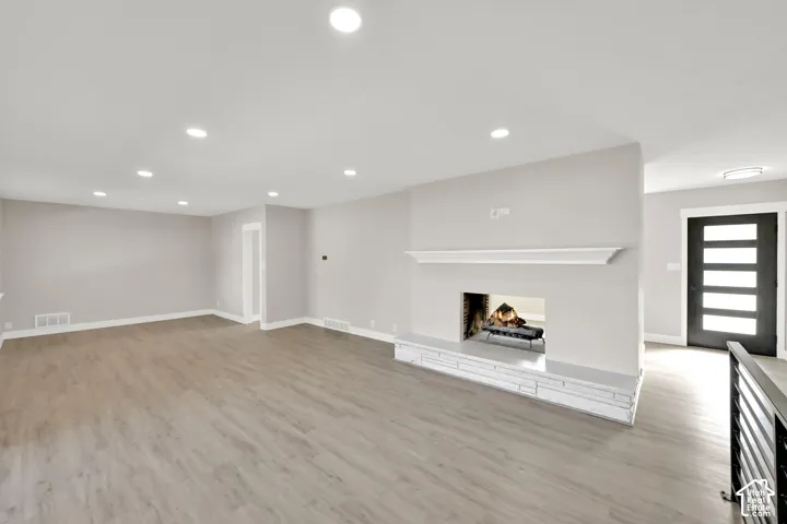 Expansive living area with recessed lighting, light wood-finish flooring, a fireplace with a stone hearth, and a contemporary entry door with frosted lites