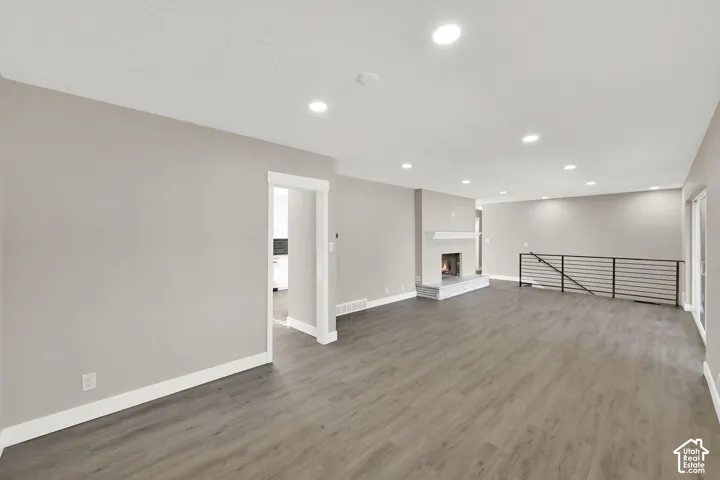 Spacious open-concept room featuring wood-finish flooring, recessed lighting, a built-in fireplace with a stone hearth, and a contemporary metal railing