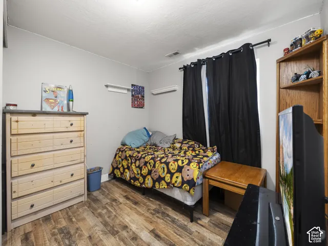 Wood-finish flooring with light gray walls, window with black curtain rods, and built-in wooden shelving