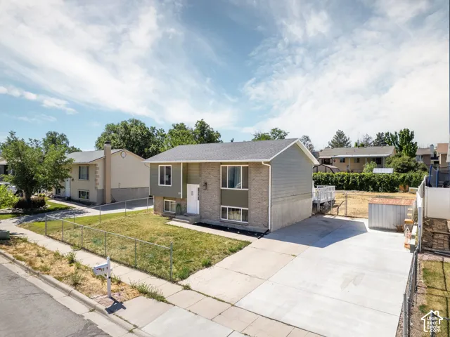 Split-level residence featuring a brick and siding exterior, a newly paved driveway, and a chain-link fence