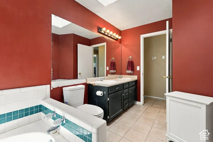 Vanity with dual sinks, overhead vanity lighting, and ceramic tile flooring