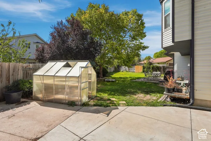 Expansive backyard featuring a well-maintained lawn, mature trees, a private fencing, and a dedicated greenhouse structure