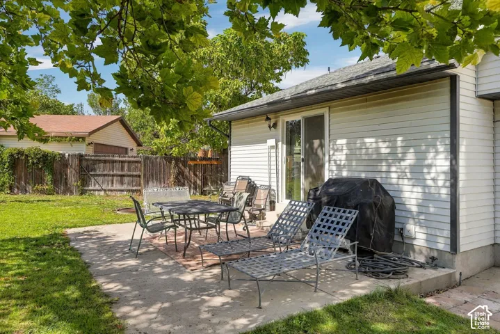 Expansive backyard featuring a concrete patio with brick inlay, a sliding glass door entry, and a wood privacy fence