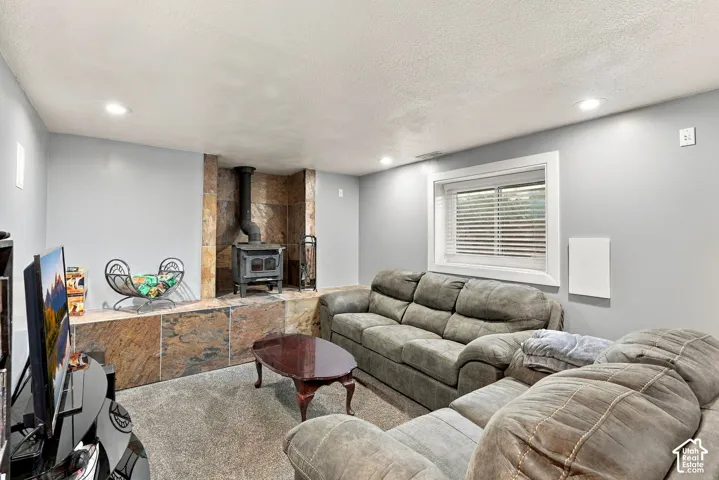 Wood-burning stove with a stone hearth and surround, recessed lighting, carpet flooring, and a single window with blinds