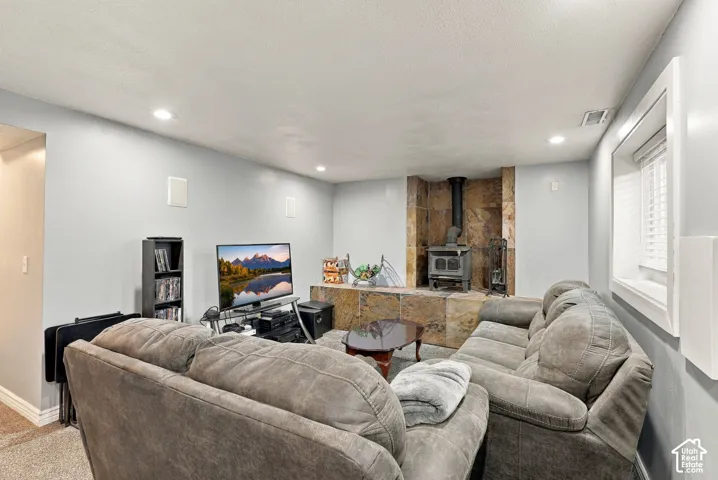 Living area featuring a stone accent wall, wood-burning stove, recessed lighting, wall-mounted speakers, and a window with blinds