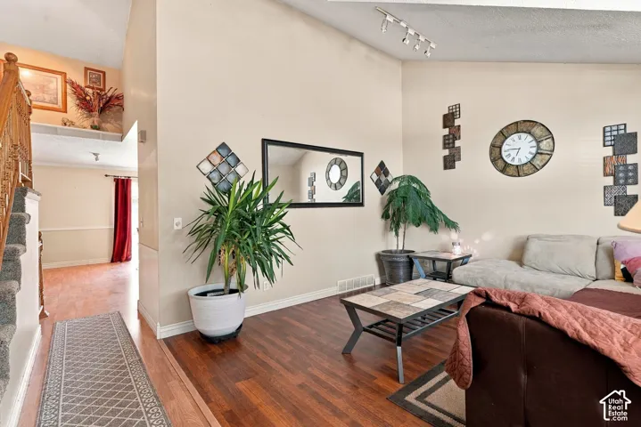 Vaulted ceiling with track lighting, wood-finish flooring, white baseboards, and built-in architectural features