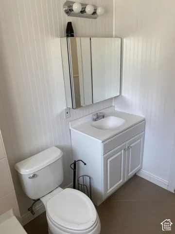 Wall-mounted vanity light with three bulbs, mirrored medicine cabinet, white vanity with two cabinet doors, integrated sink, and white toilet