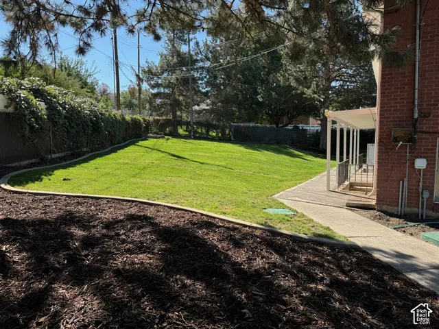 Expansive green lawn, mulched planting beds, mature perimeter trees, paved patio, and brick exterior