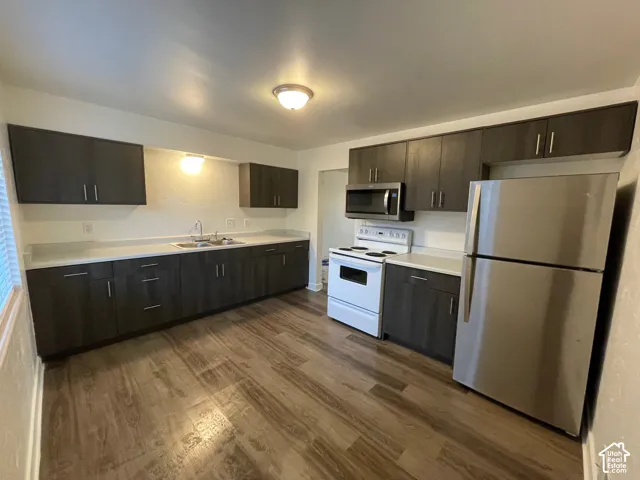 Kitchen featuring wood-finish flooring, dark wood-finish cabinetry, light-toned countertops, and stainless steel appliances