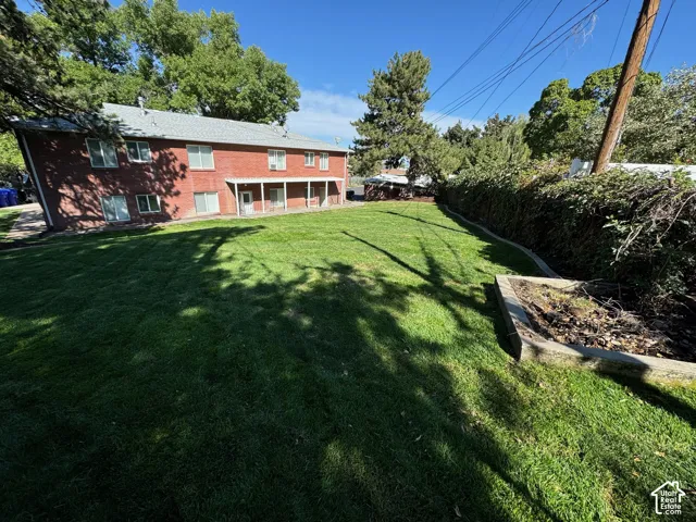 Expansive green lawn with mature perimeter trees, brick exterior, and covered patio