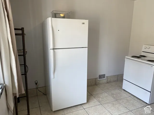 White two-door refrigerator, white electric range, and light-toned tile flooring