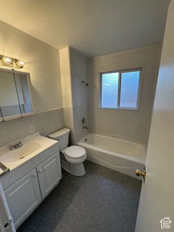 Full bathroom featuring a single vanity with storage, a white toilet, a white bathtub with a shower, textured wall tile, and a window for natural light