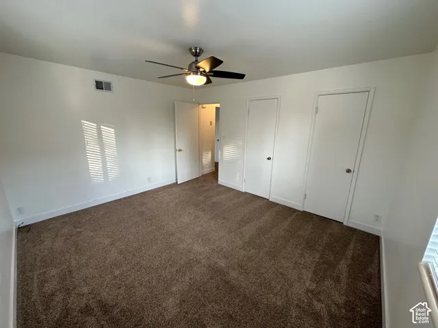 Textured carpet flooring, white walls, and a ceiling fan with integrated lighting