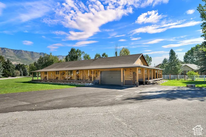 Log cabin exterior with a covered porch, attached garage, paved driveway, and mountain views