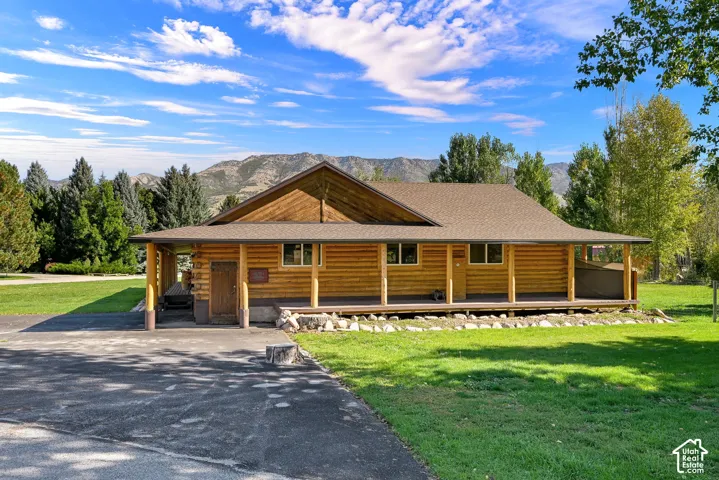 Log cabin exterior with a covered porch, attached garage, paved driveway, and mountain views