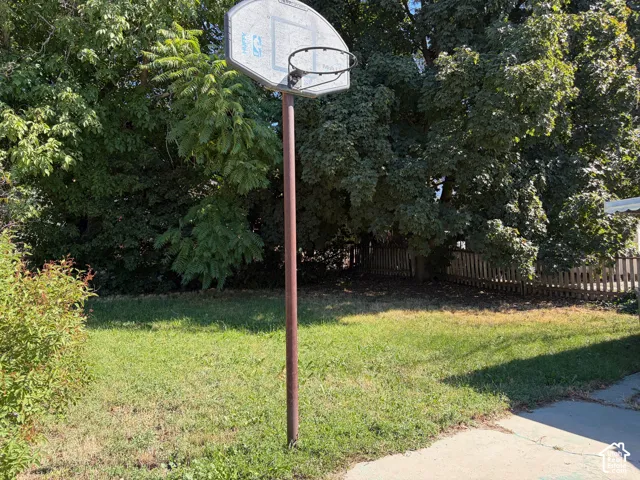 Expansive green space featuring a basketball hoop, established trees, and a wooden fence