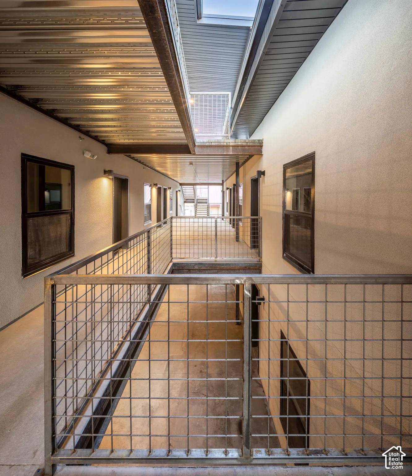 Corrugated metal ceiling, exposed beam, grid-patterned metal railings, and natural light from skylight