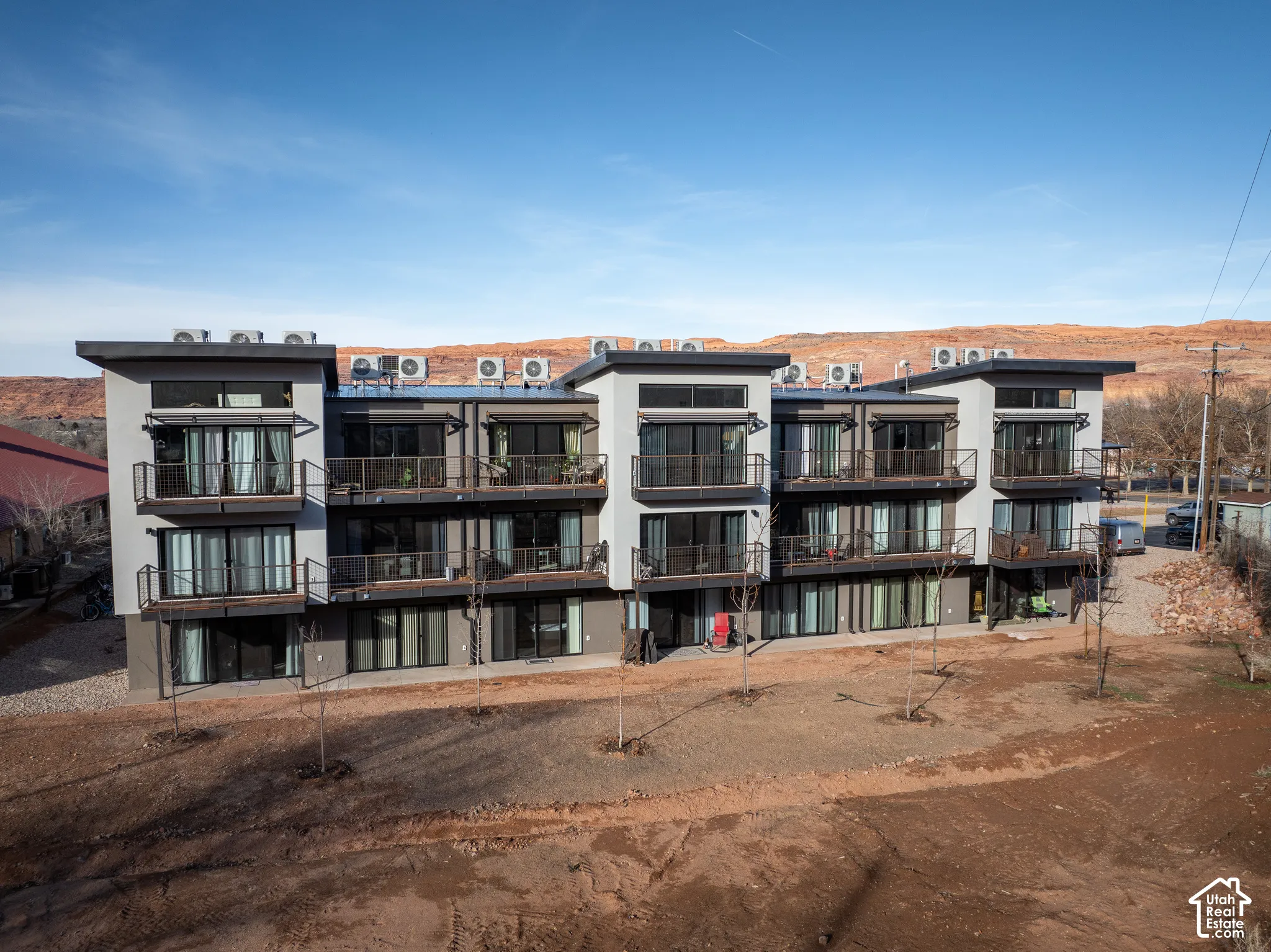 Multi-story building featuring modern architecture with balconies on upper levels, ground-level patios, and a contemporary flat roof design