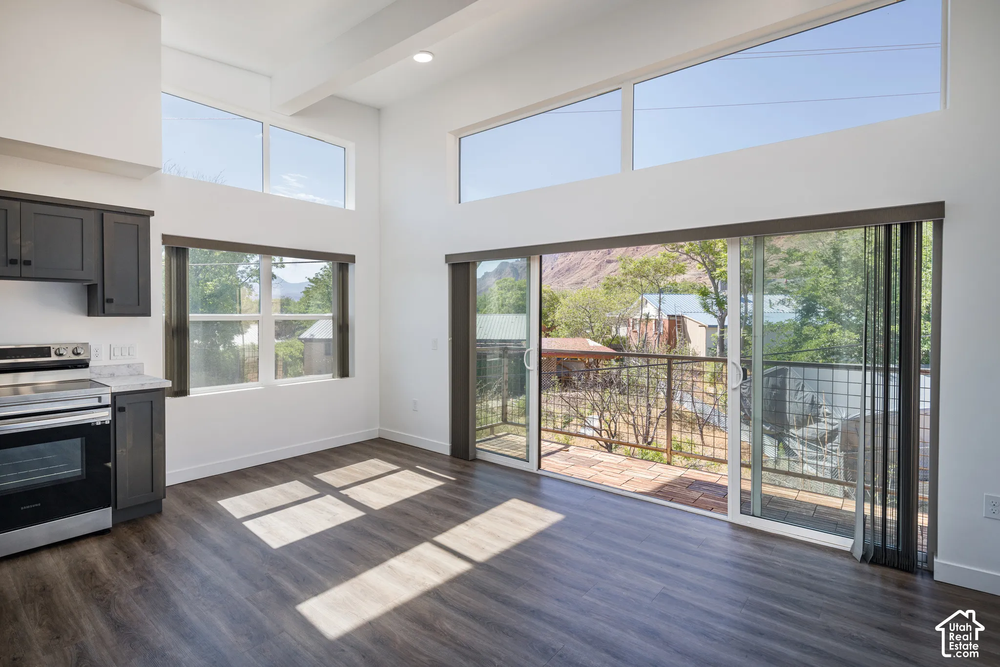 High vaulted ceilings, abundant natural light from transom and large pane windows, wood-finish flooring, and a sliding glass door opening to an exterior balcony