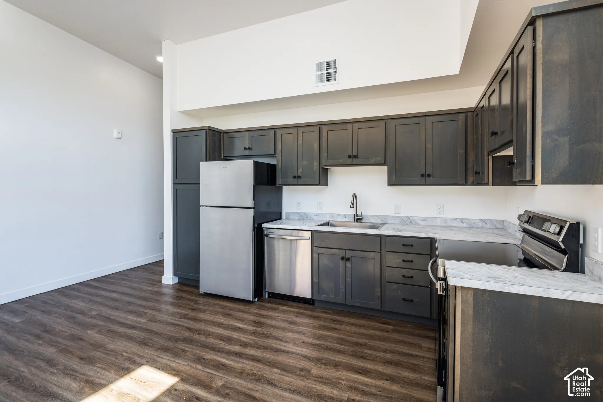 Kitchen featuring wood-finish flooring, dark-stained cabinetry, light-toned countertops, and stainless steel appliances