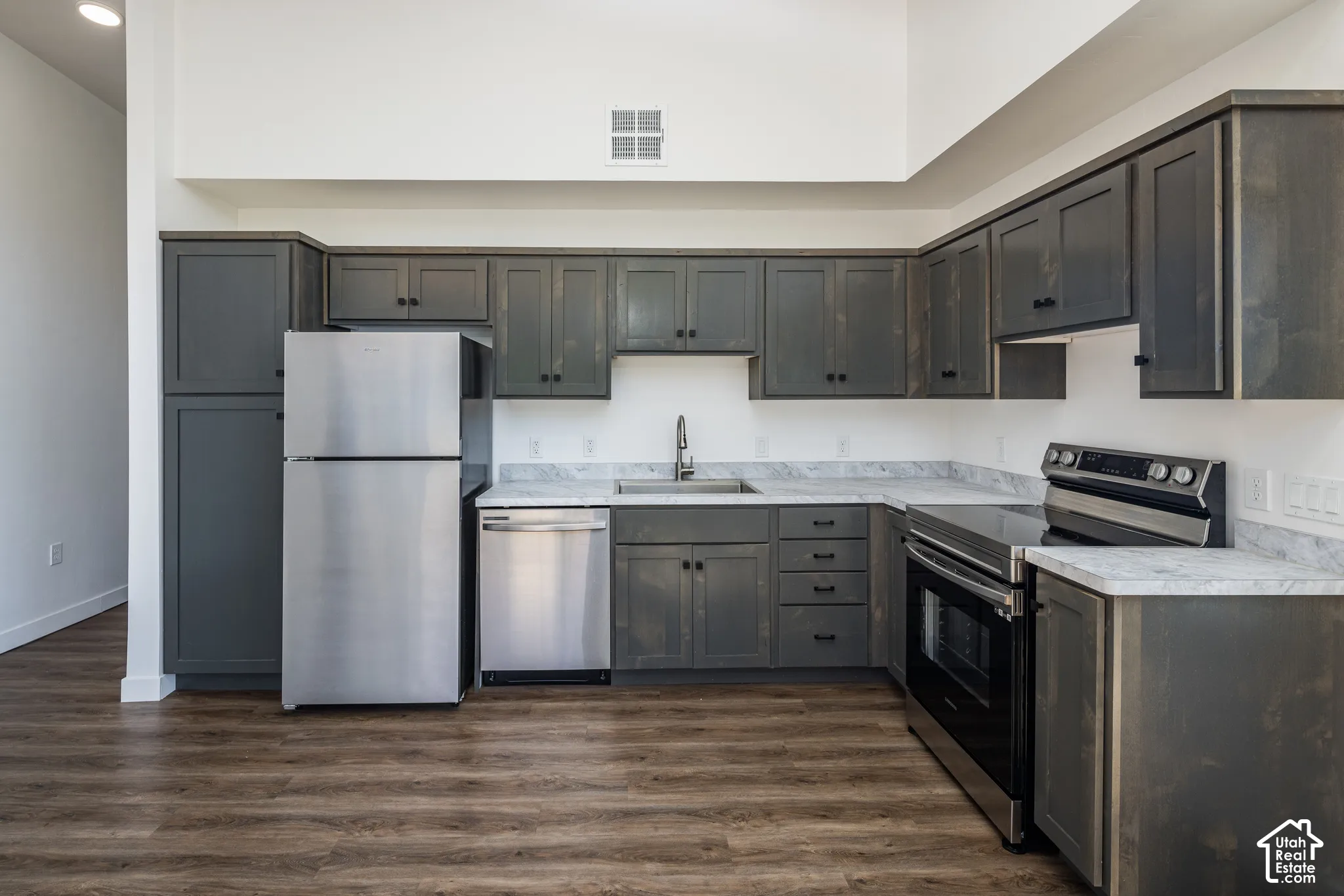 Kitchen featuring dark wood-finish cabinetry, light-toned countertops, stainless steel appliances, and wood-finish flooring